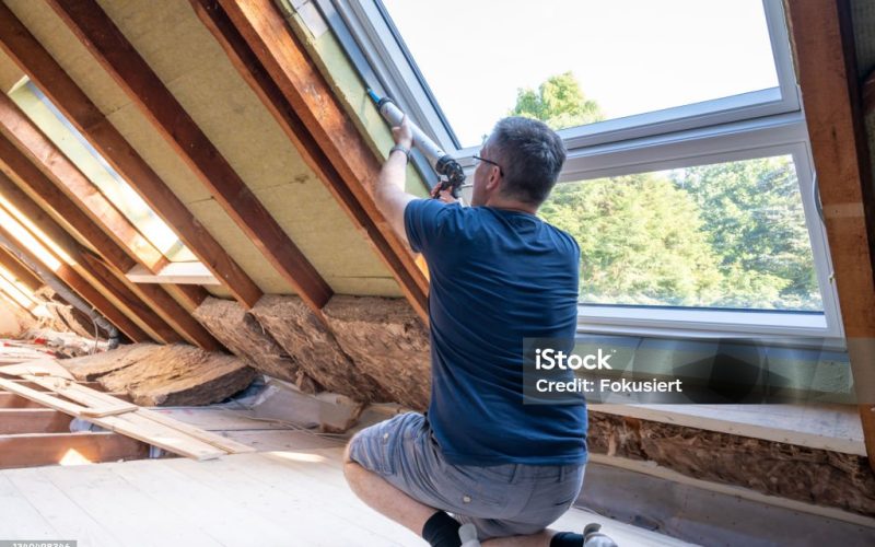Craftsman caulking a new window in the attic.